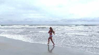 Gün batımında okyanus kıyısında koşan bir kadın. Drone videosu.