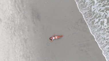 Okyanus sörfünün yanındaki kumlu sahilde mayo giymiş bir kadın. Drone görünümü.