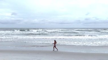 Genç bir kadın okyanus boyunca ağır çekimde koşuyor, yukarıdan vurulmuş. Spor yaşam tarzı, spor ya da seyahat.