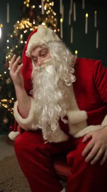 Noel Baba kostümü giyen yorgun bir adam uzun bir iş gününden sonra dinleniyor ve tatil sezonunun komik ve gerçekçi tarafını yakalıyor. Dikey video.