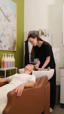 Profesyonel kuaför kadın müşterinin saçını yıkıyor. Güzellik salonunda sandalyede yatıyor. Rahatlatıcı şampuan ve saç bakımı prosedürü.