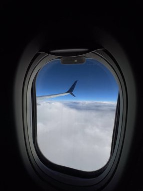 Bir uçak penceresinden büyüleyici bir manzara. Mavi gökyüzü ve bulutların arka planına karşı bir kanat sergiliyor..