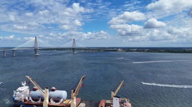 Çarpıcı bir hava manzarası karayı suyun üzerine bağlayan bir köprü gösteriyor. Yakındaki kargo gemileri kenetlenmiş, ticareti vurguluyor.