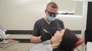 Bir dişçi, modern ve çağdaş bir diş muayenehanesi içindeki bir hastaya aktif olarak diş tedavisi uygular..