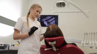 Modern bir klinikte diş muayenesi sırasında bir dişçi ve hasta. Sahne oral sağlık, tıbbi danışmanlık ve profesyonel tedavi planlamasını vurguluyor.