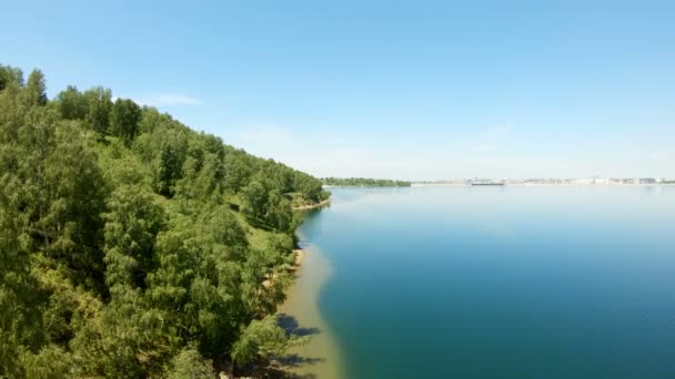 Дрон летить над водою вздовж зеленого берега до міста — стокове відео