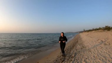 Gün batımında kumlu plajda koşan kadın koşucu