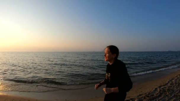 Vrouwelijke runner joggen op het zandstrand bij zonsondergang — Stockvideo