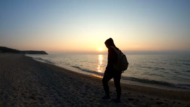 En man går längs stranden vid solnedgången — Stockvideo