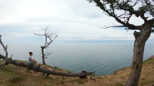 Chica sentada en un árbol en la orilla del lago Baikal — Vídeo de stock