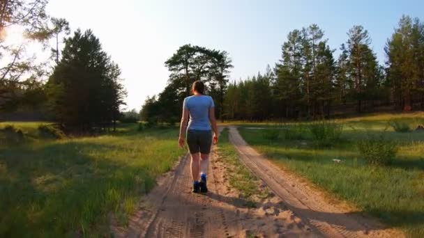 Девушка под солнцем, идущая по проселочной дороге на закате — стоковое видео