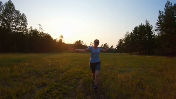 Chica sonriente alegre, brazos levantados corriendo por el campo al atardecer — Vídeos de Stock