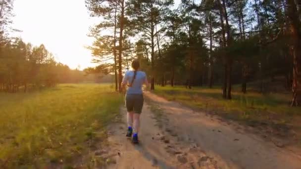 Девушка бежит по проселочной дороге на закате — стоковое видео