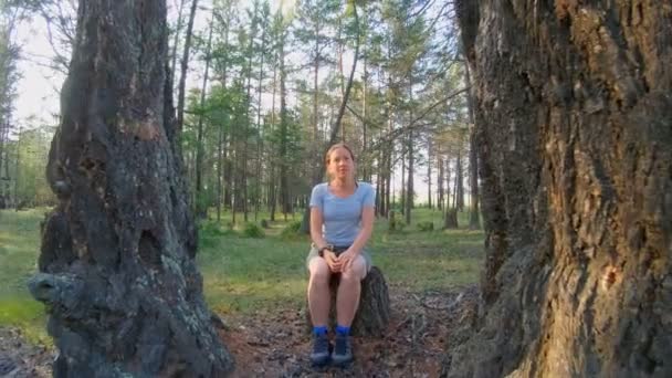 Девушка сидит на пне между двумя большими деревьями в лесу — стоковое видео