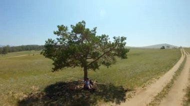 Kız bir köy yolu yakınındaki bir alanda bir ağacın altında oturan ve çizer. Havadan görünüm