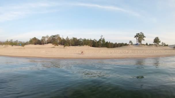 Drone voa sobre a água em direção à costa atirando em uma menina sentada na praia desenho — Vídeo de Stock