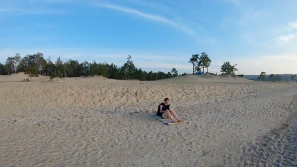 Chica sentada en la playa de arena y dibujando un paisaje. Gimbal tiro — Vídeos de Stock