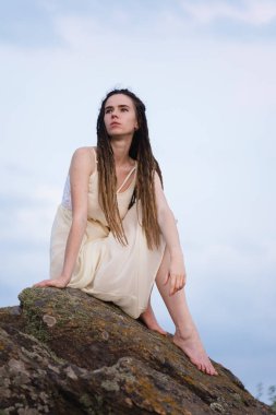 Işığı elbiseyle bir kayaya oturan güzel kız.