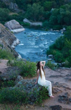 Işığı elbiseyle bir kayaya oturan güzel kız