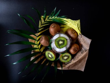 Siyah bir arka planda Hindistan cevizi, kivi ve palmiye dallar benzersiz şenlikli buket. Meyve buketi. Sağlıklı konsept meyve ve sebzeler.