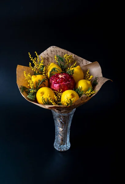 Unique festive bouquet of pomegranate, lemon and memoses on a black background. Fruit bouquet. Fruits and Vegetables of the Healthy Concept.