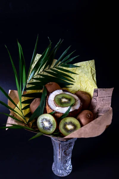 Unique festive bouquet of coconut, kiwi and palm twigs on a black background. Fruit bouquet. Fruits and Vegetables of the Healthy Concept.