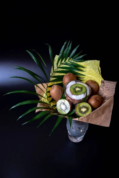 Unique festive bouquet of coconut, kiwi and palm twigs on a black background. Fruit bouquet. Fruits and Vegetables of the Healthy Concept.