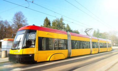 Modern şehir demiryolu taşımacılığı. Şehirde hareket bulanıklığı etkisi olan sarı tramvay hızlı hareket eder. Demiryolunda yüksek hızlı yolcu treni hareket halinde. Gündüz vakti caddede hareket eden sarı tramvay bulanıklaştı