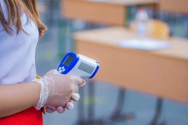 Una chica con guantes sostiene un termómetro electrónico para comprobar la temperatura. Control de temperatura para prevenir la propagación del coronavirus. Imágenes de stock libres de derechos