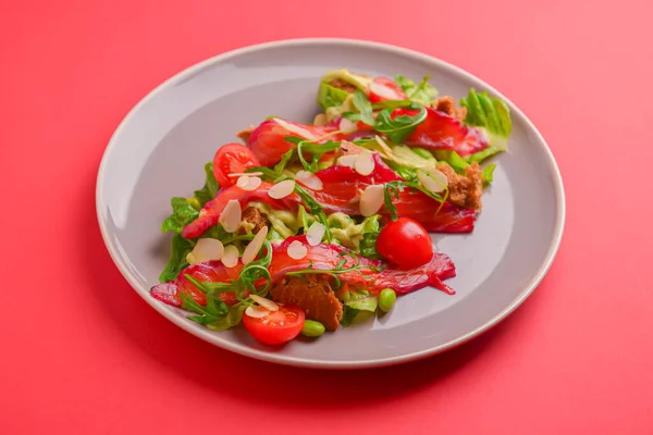 Salada fresca com salmão salgado defumado, tomates e sementes de abóbora. Servido em uma placa cinza sobre fundo vermelho brilhante . — Fotografia de Stock