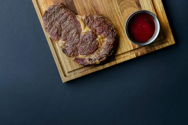 Bife de carne fresca e temperos em tábua de madeira rústica sobre fundo preto. Vista superior, flat lay, copiar banner espaço . — Fotografia de Stock