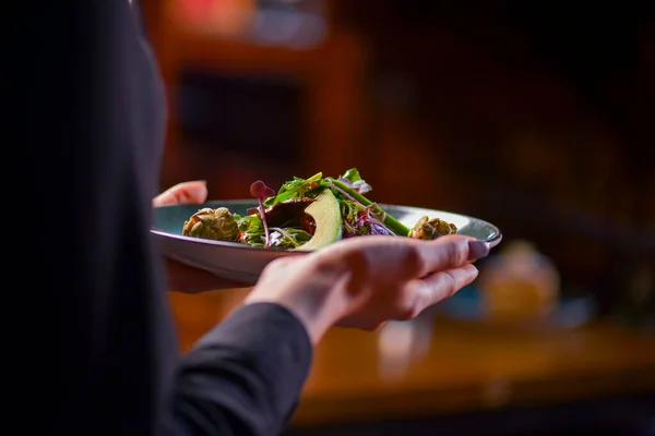 Garçom em uniforme preto, camisa, trazendo o espinafre saudável ordenado e salada de arugula com abacates . — Fotografia de Stock