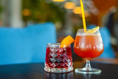 Two colorful refreshing cocktails served on a dark rustic wooden table with blurred background.