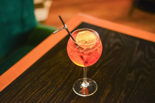 Cóctel de alcohol frío de verano con hielo y naranja en un vaso alto sobre una mesa de madera sobre fondo borroso del restaurante . — Foto de Stock