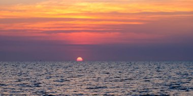 Huzurlu deniz manzarasının üzerinde gün batımı. Sakin denizin üzerinde güzel bulutlu bir gökyüzü ve güneş ışığı yansıması. Boşluk afişini kopyala.