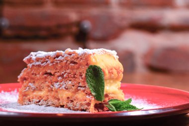 Kırsal ahşap arka planda kırmızı tabakta dilimlenmiş ballı kek. Ev yapımı pişirme..