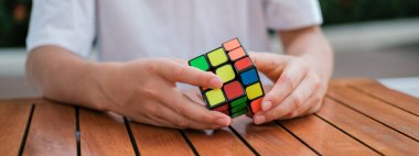 Rubiks küpünü tutan ve masada oynayan sevimli çocuk portresi. Rubiks küpü çocukların elinde. Pankart.