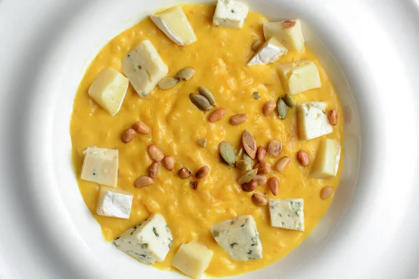 Kabak çekirdeği ve peynirle kaplı kremalı balkabağı çorbası ahşap bir masada, ekose masa örtüsüyle.. — Stok fotoğraf