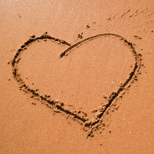 Heart drawn on sand, seacoast. Golden sand beach close up, summer holidays border frame concept.