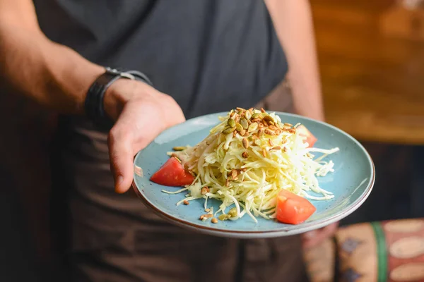 Ayçekirdeği ve domatesli lahana salatası. Mavi tabakta servis edilmiş. Bir garsonun elinde. Restoran servisi..