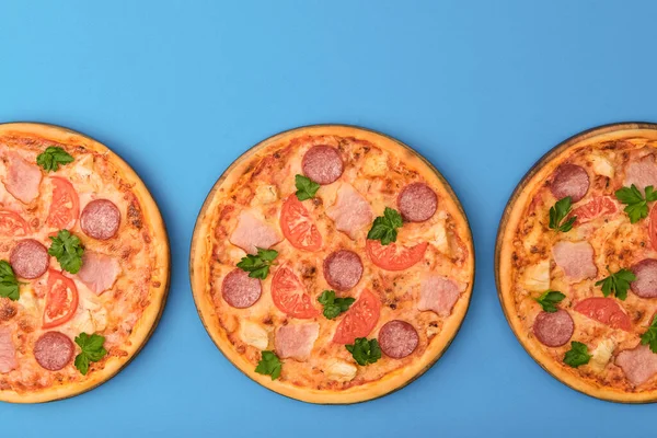 Three pizzas on the blue azure background. Pizza isolated. Banner with copy space for text or logo. Italian cuisine.