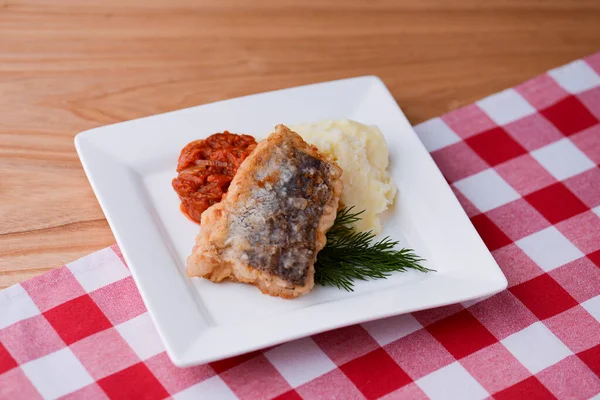Stekt fisk och potatismos med dill och sås serveras på en vit tallrik över ljus trä bord bakgrund. — Stockfoto