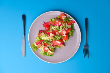 Taze salata, füme tuzlu somon, domates ve kabak çekirdeği. Gri dokuda gri bir tabakta servis edilir..