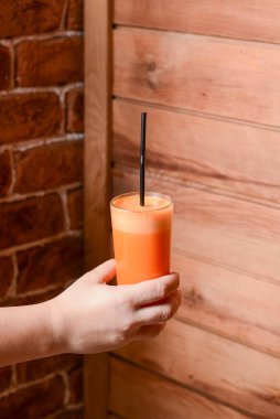 Bir garson bir bardak portakal suyu tutar. Kafede garsonun elinde bir bardak meyve suyu. Ahşap arkaplan.