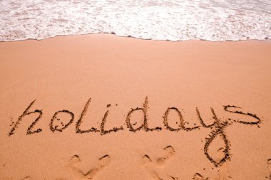 Tatiller el yazısıyla kumda deniz dalgası ile yazılır. Yazın kumsaldaki kum dokusunu kapat. Tatil, tatil konsepti, boş plaj. Pankart.