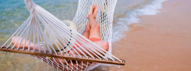 Kumsaldaki hamakta yatan kumlu ayaklı çocuk. Deniz kıyısındaki tropik sahilde sıcak bir hamak. Huzurlu deniz manzarası. Sakin denizin üzerindeki güzel mavi gökyüzü ve güneş ışığı yansıması. Boşluk afişini kopyala.