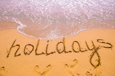 Tatiller el yazısıyla kumda deniz dalgası ile yazılır. Yazın kumsaldaki kum dokusunu kapat. Tatil, tatil konsepti, boş plaj. Pankart.