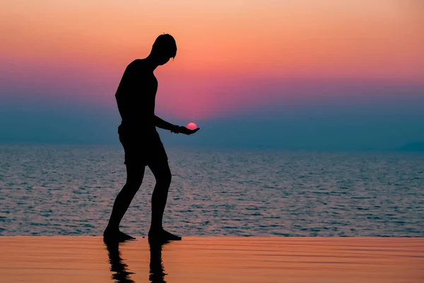 一个在游泳池里享受日落的小男孩 夕阳西下的人物形象 手握太阳 复制太空横幅 美丽的天空背景 — 图库照片