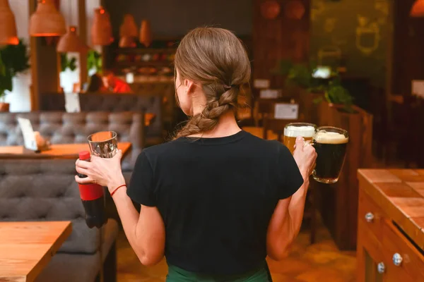 Beautiful young woman waiter with beer in the hands in a pub or bar serving beer and water