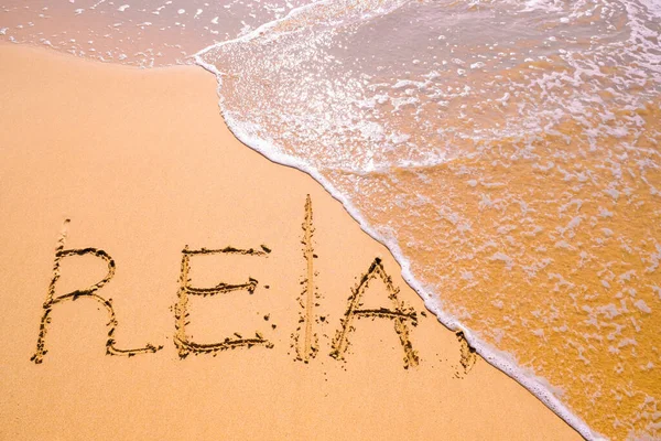 Word Relax hand written in the sand with a sea wave. Close up sand texture on beach in summer. Vacation, holiday concept, empty beach. Banner.